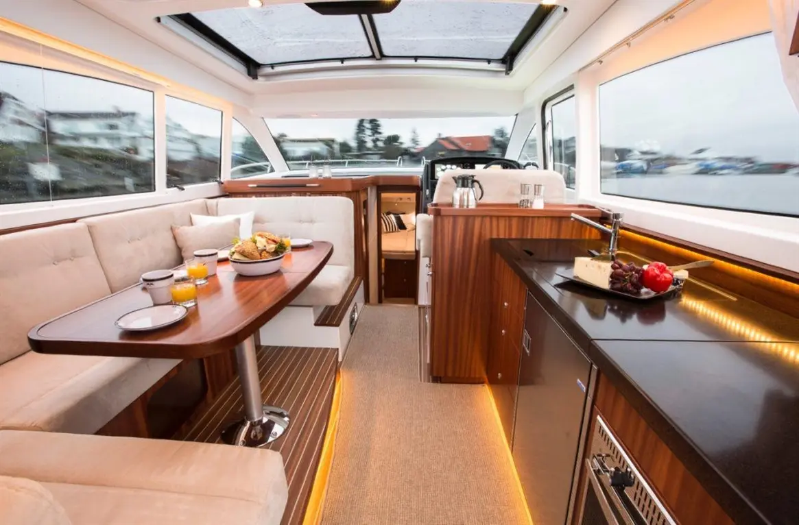 Stylish boat interior featuring a dining area with food, drinks, and a well-equipped kitchen, all with modern finishes.
